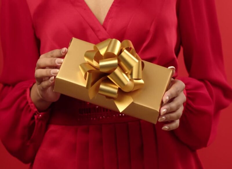 devojka drži poklon umotan u zlatnu foliju u ruci