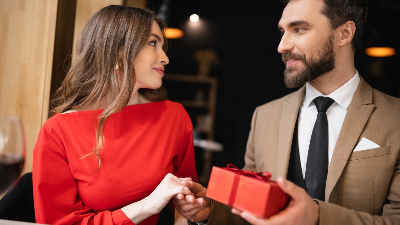 Muškarac poklanja ženi elegantno upakovan poklon dok se gledaju i smeše